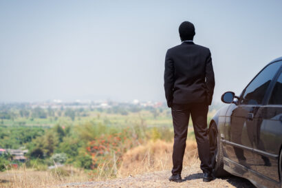 African Businessman standing on top of rock cliff with car