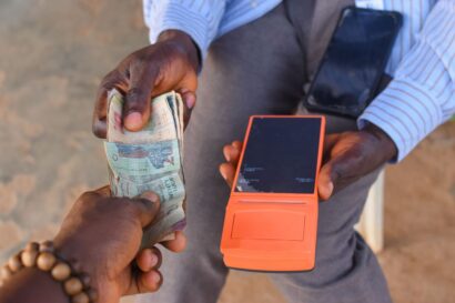 Hands of two african individuals doing financial transaction with a point of sales POS terminal as Cash, Naira, Money or currency is changing hands