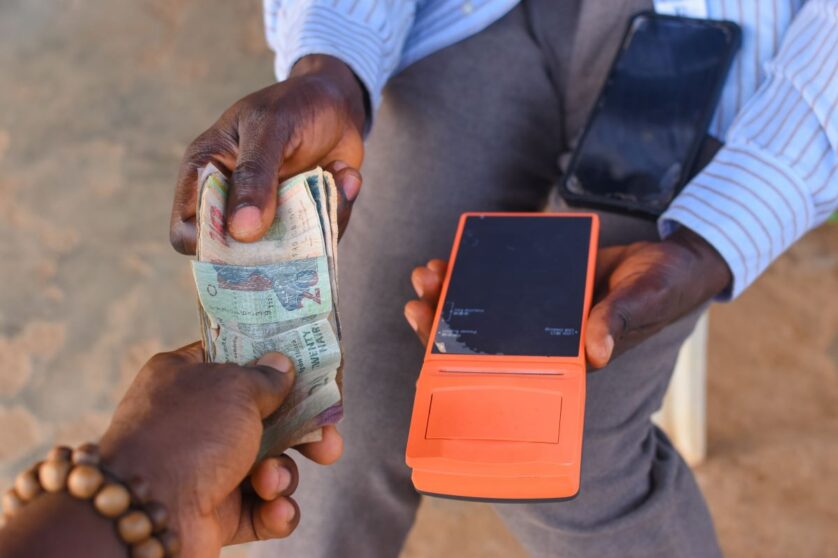 Hands of two african individuals doing financial transaction with a point of sales POS terminal as Cash, Naira, Money or currency is changing hands