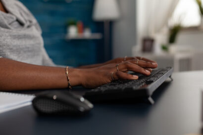 Close up of hands using keyboard to work on computer at desk. Young woman working on business project with modern device and technology at home, browsing online internet webiste.