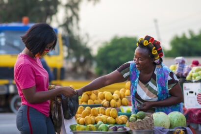A woman buys fruit from a female vendor at an open market.