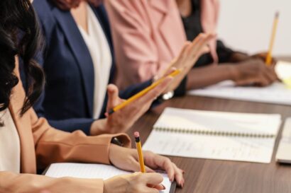 Close up shot of a team of three women working with notebooks open on a wooden table but no faces shown.