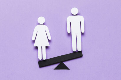 A cartoon image of a woman standing on the lower side of a seesaw opposite a man, against a light purple background.