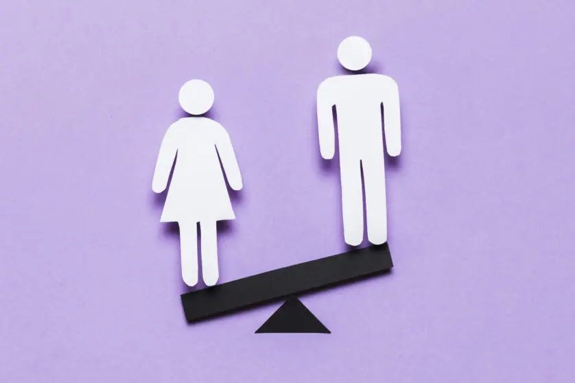 A cartoon image of a woman standing on the lower side of a seesaw opposite a man, against a light purple background.