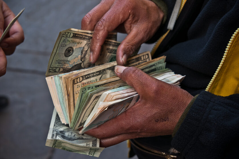 Close up on the hands of a man holding a stack of money including US dollar bills.