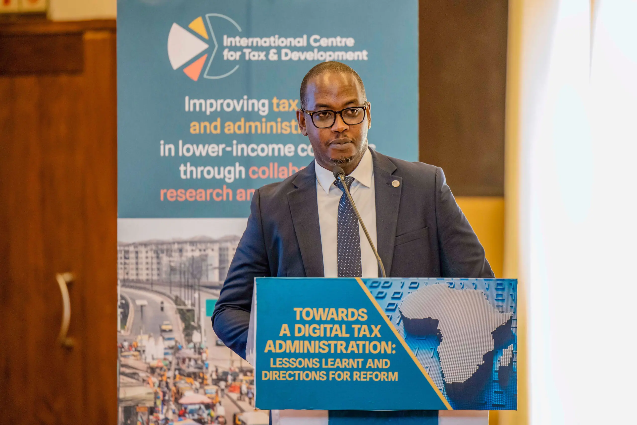 Medium shot of a Rwandan man in a suit giving a speech in front of a lectern