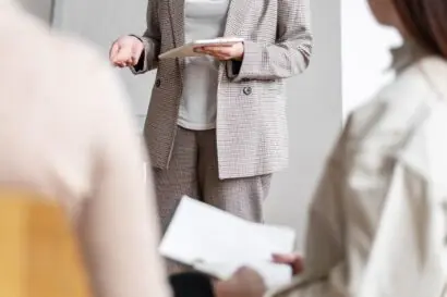 Close up shot of a women from the chest down presenting to an audience seen only from the back