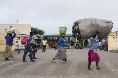 Des gens, y compris des femmes portant des objets lourds sur la tête, passent devant un dépôt d’autobus, près du marché de Kantamanto, tôt le matin sur une route au centre-ville d’Accra.