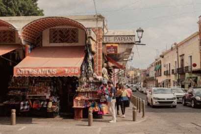 Wide shot of a small artisan store in Mexico, with a small crowd of people gathering to check the displayed items.