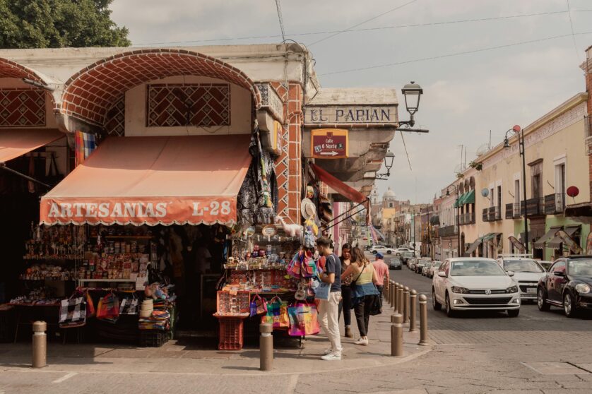 Wide shot of a small artisan store in Mexico, with a small crowd of people gathering to check the displayed items.