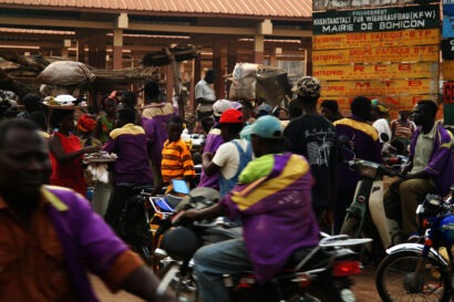 In action shot of a busy street near a market in Bohicon, Benin, West Africa with people on motorbikes or walking.