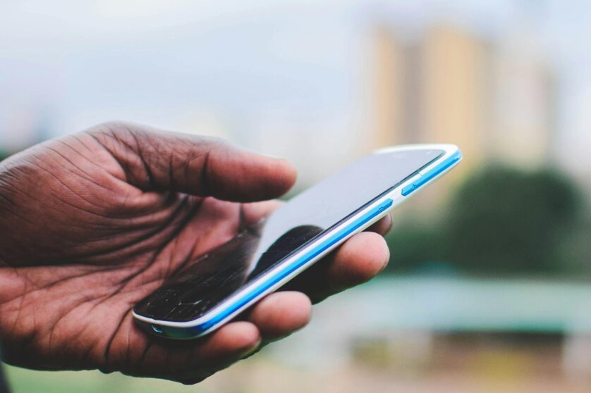 Close up on a hand of an Africa person from Kenya, holding a phone to access digital services.