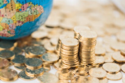 A quarter of a globe on top of a pile of gold coins beside three uneven stacks of coins.