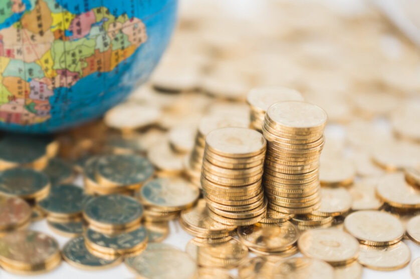 A quarter of a globe on top of a pile of gold coins beside three uneven stacks of coins.